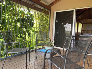 A covered outdoor seating area with metal chairs and a table, surrounded by a metal fence and greenery.
