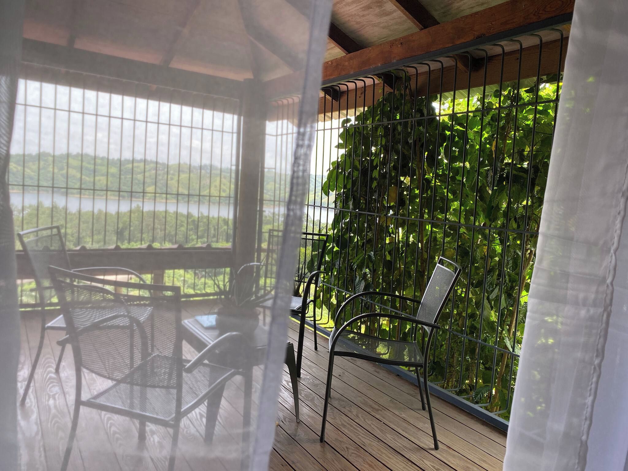 A covered outdoor seating area with metal chairs and a view of a lake through a metal fence.