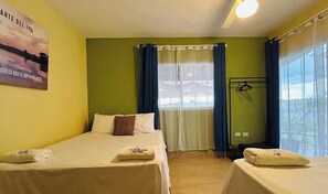 Habitación de hotel con dos camas, una ventana con cortinas, un perchero en la pared y un cartel en la pared.