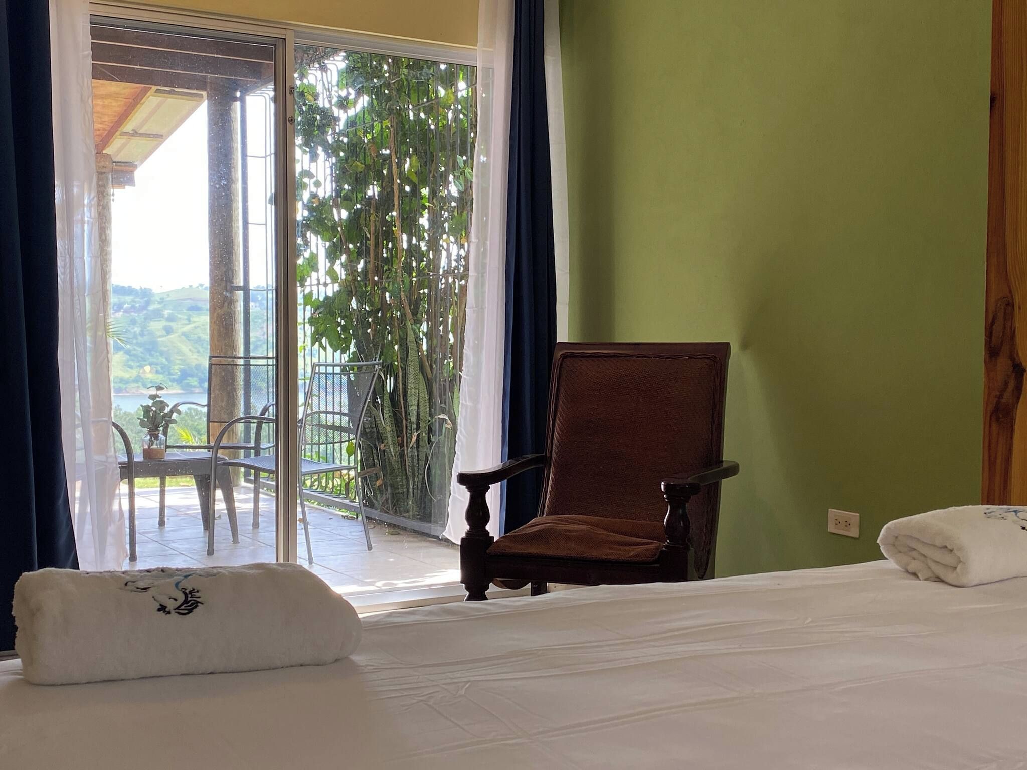 A hotel room with a bed, a chair, and a view of a balcony with greenery.