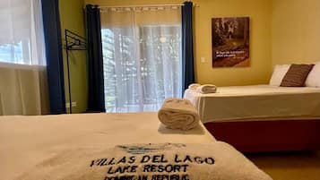 A hotel room with a bed, a window with curtains, a wall with a poster, and a towel on the bed.