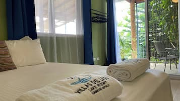 A hotel room with a bed, a window with curtains, a view of greenery outside, and a towel with text on it.