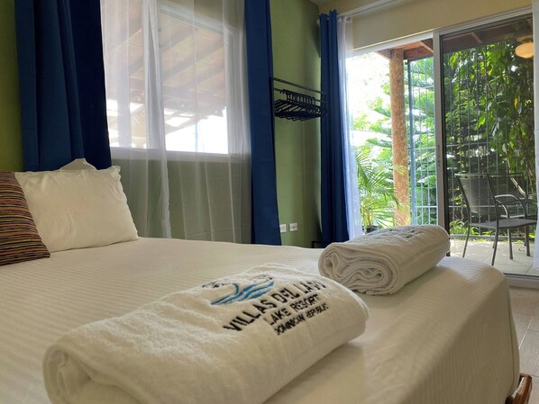 A hotel room with a bed, a window with curtains, a view of greenery outside, and a towel with text on it.
