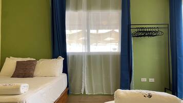 Una habitación con cama, un banco, una ventana con cortinas y un tendedero de pared.