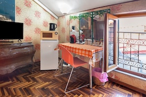 A compact room with a wooden herringbone floor, a television, a microwave, a refrigerator, a table with a checkered tablecloth, a red chair, and a window with decorative iron bars. - Room 'Camera Singola' with Wi-Fi (Grosseto)