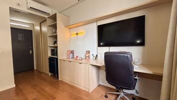 Habitación de hotel compacta con kitchenette, televisor de pantalla plana en la pared, escritorio con silla y un pequeño rincón de descanso.