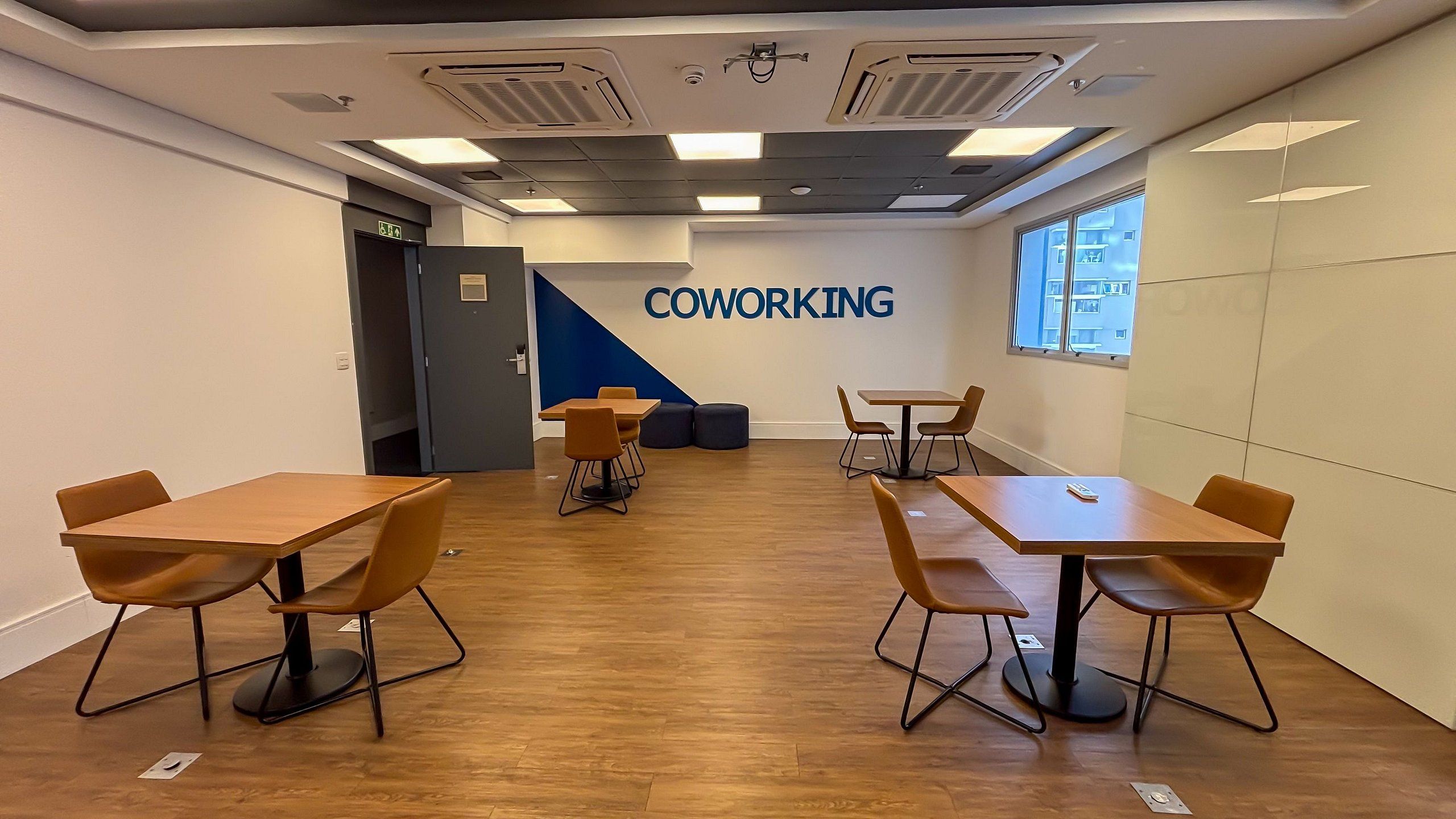 Un espace de coworking doté de plusieurs tables et chaises, d’un mur d’accent bleu et d’une fenêtre laissant entrer la lumière naturelle.