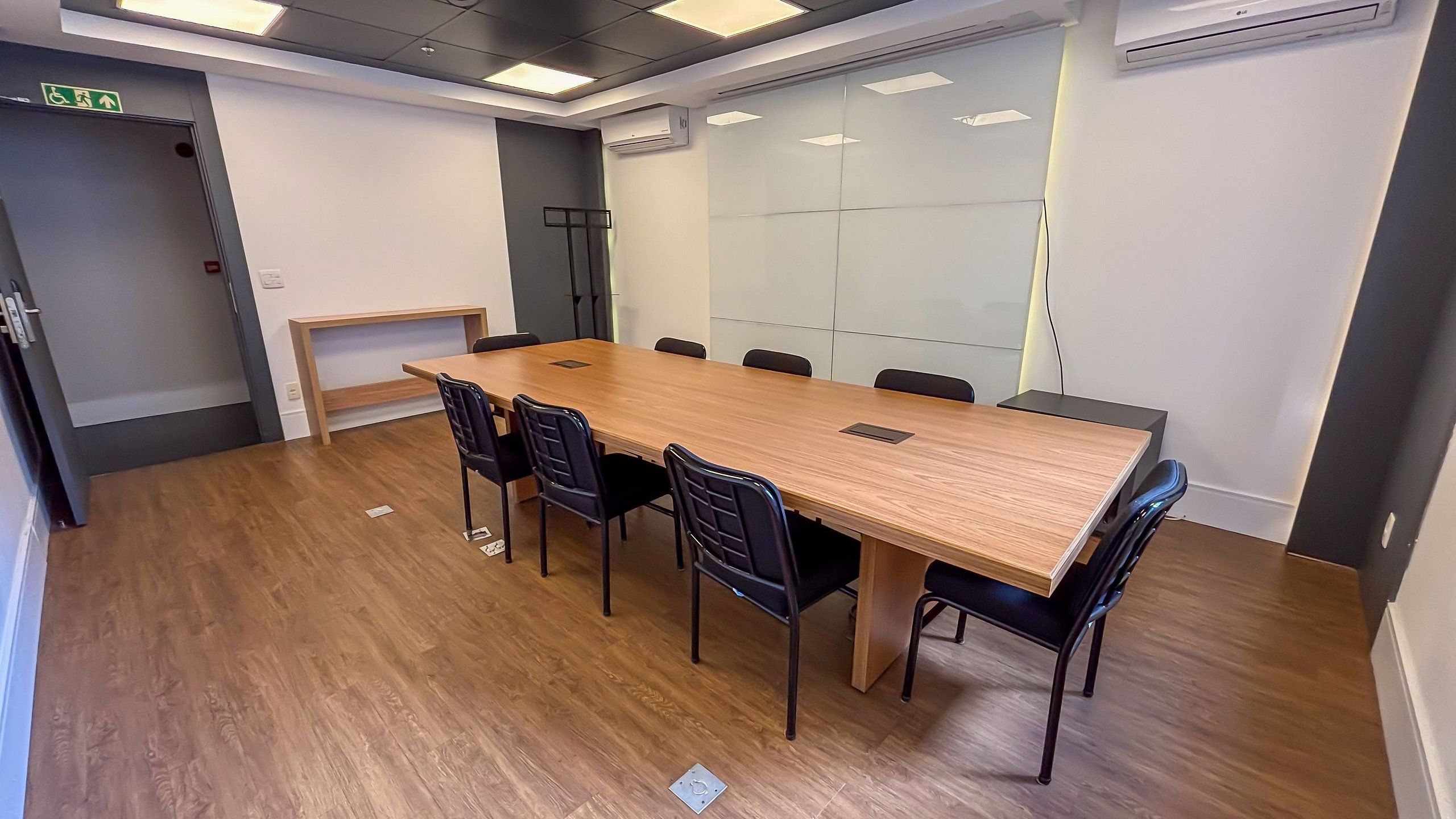 A conference room with a long table, black chairs, a whiteboard, and a glass partition wall.