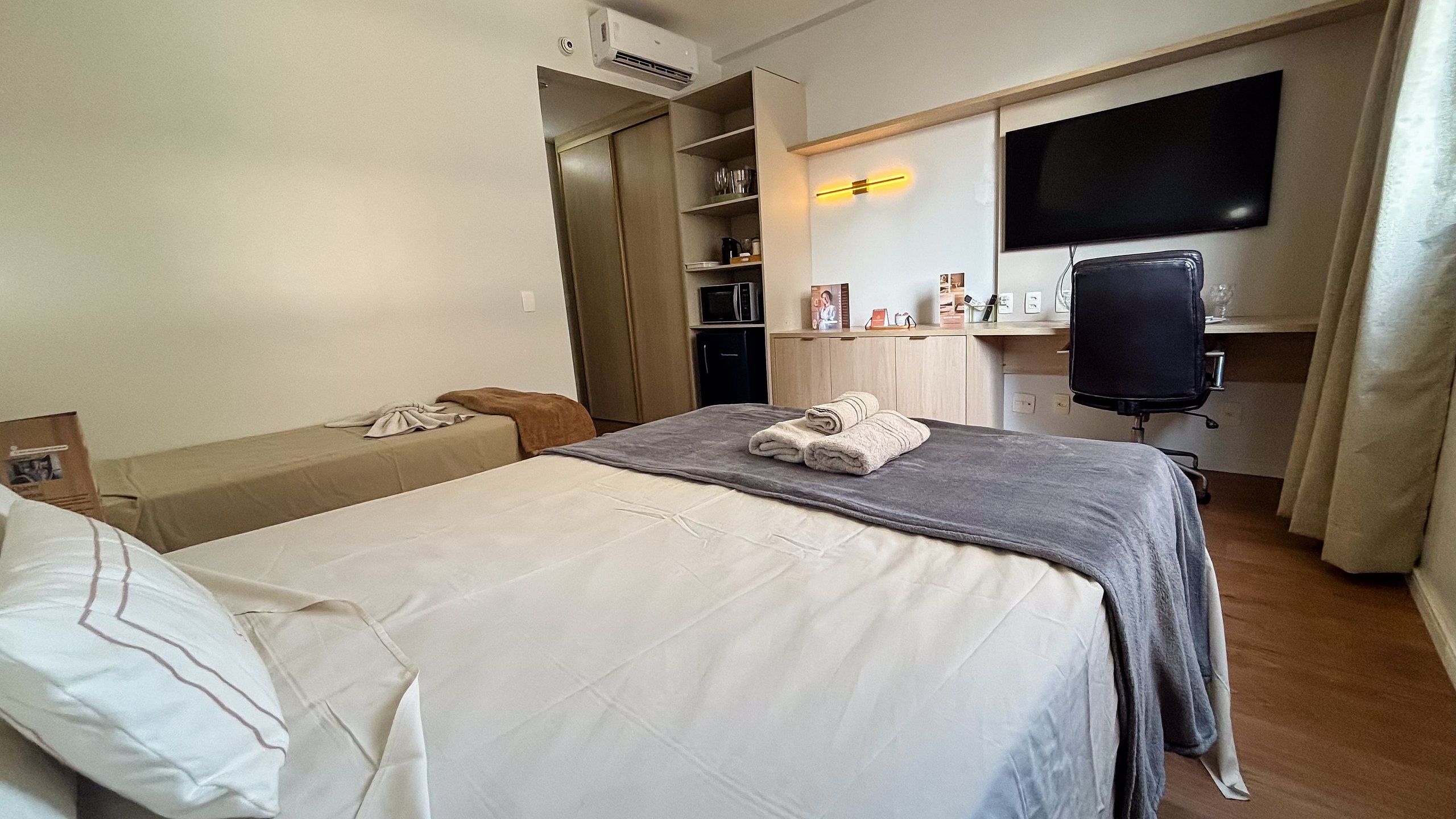 Una habitación de hotel con cama, escritorio, silla, televisor y armario.