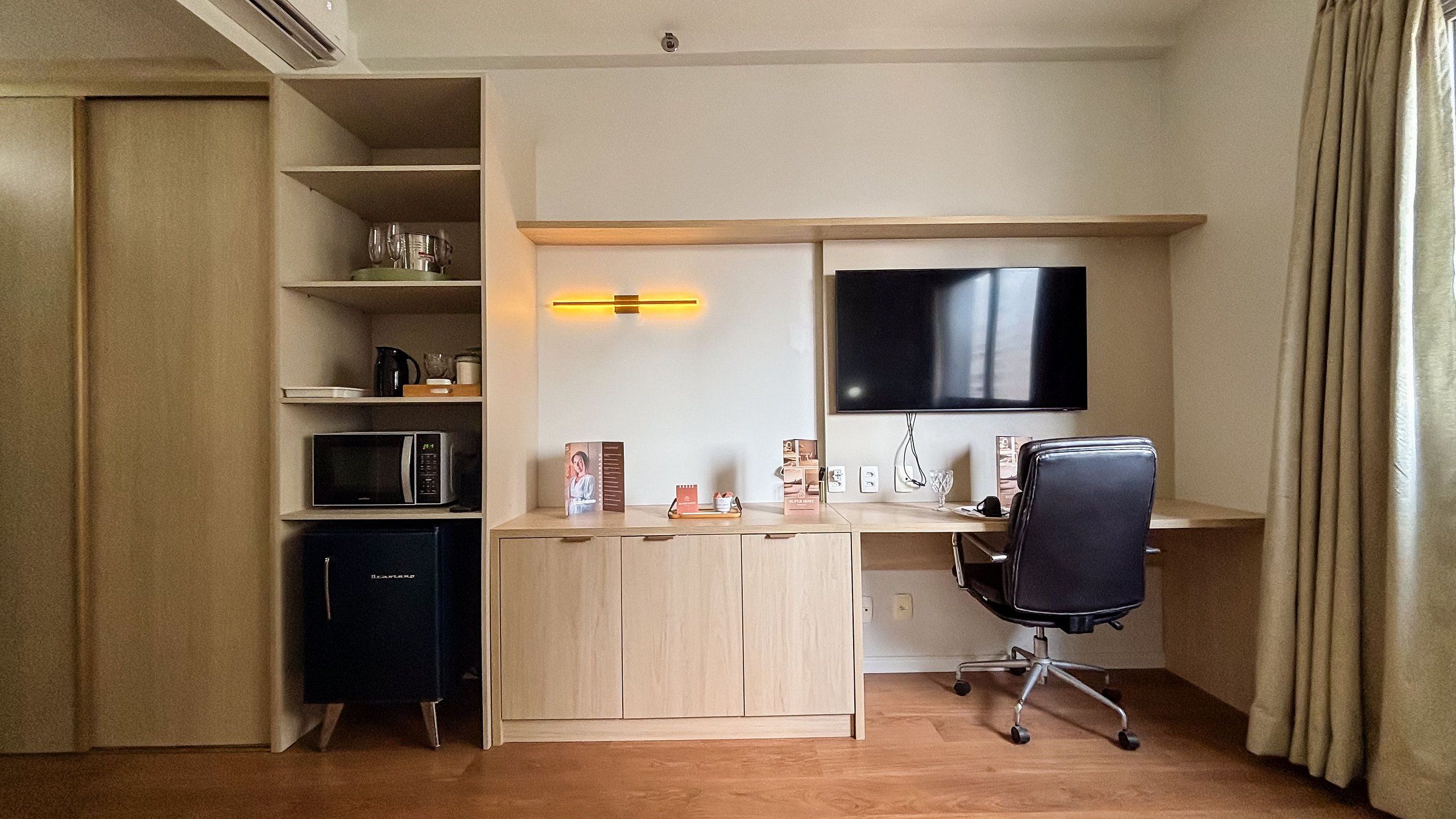Habitación de hotel compacta con kitchenette, escritorio con silla, televisor de pantalla plana y cama.
