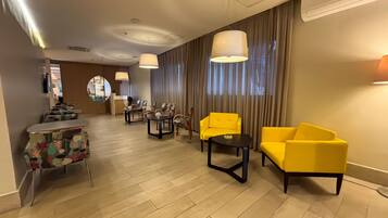 A hotel lobby with a reception desk, seating area, and a staircase leading to another floor.