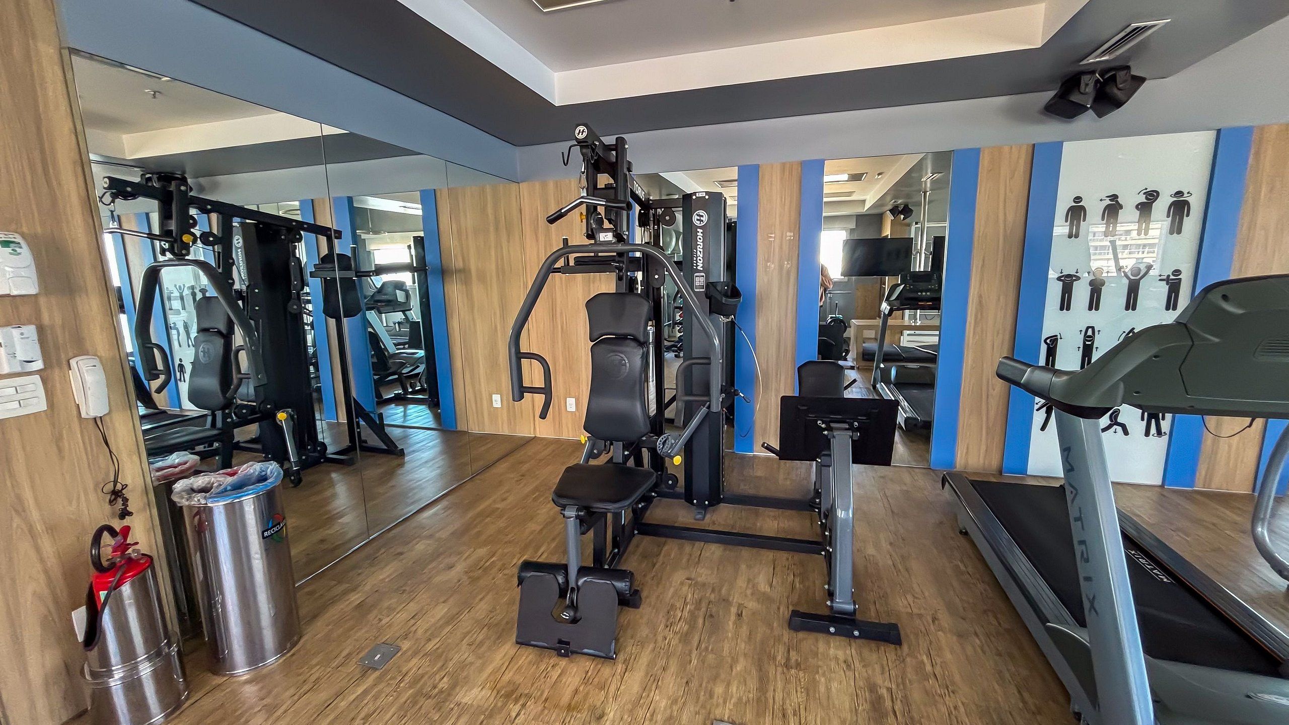 Une salle de sport équipée de matériel d’exercice, d’un tapis de course et d’un mur recouvert de miroirs.