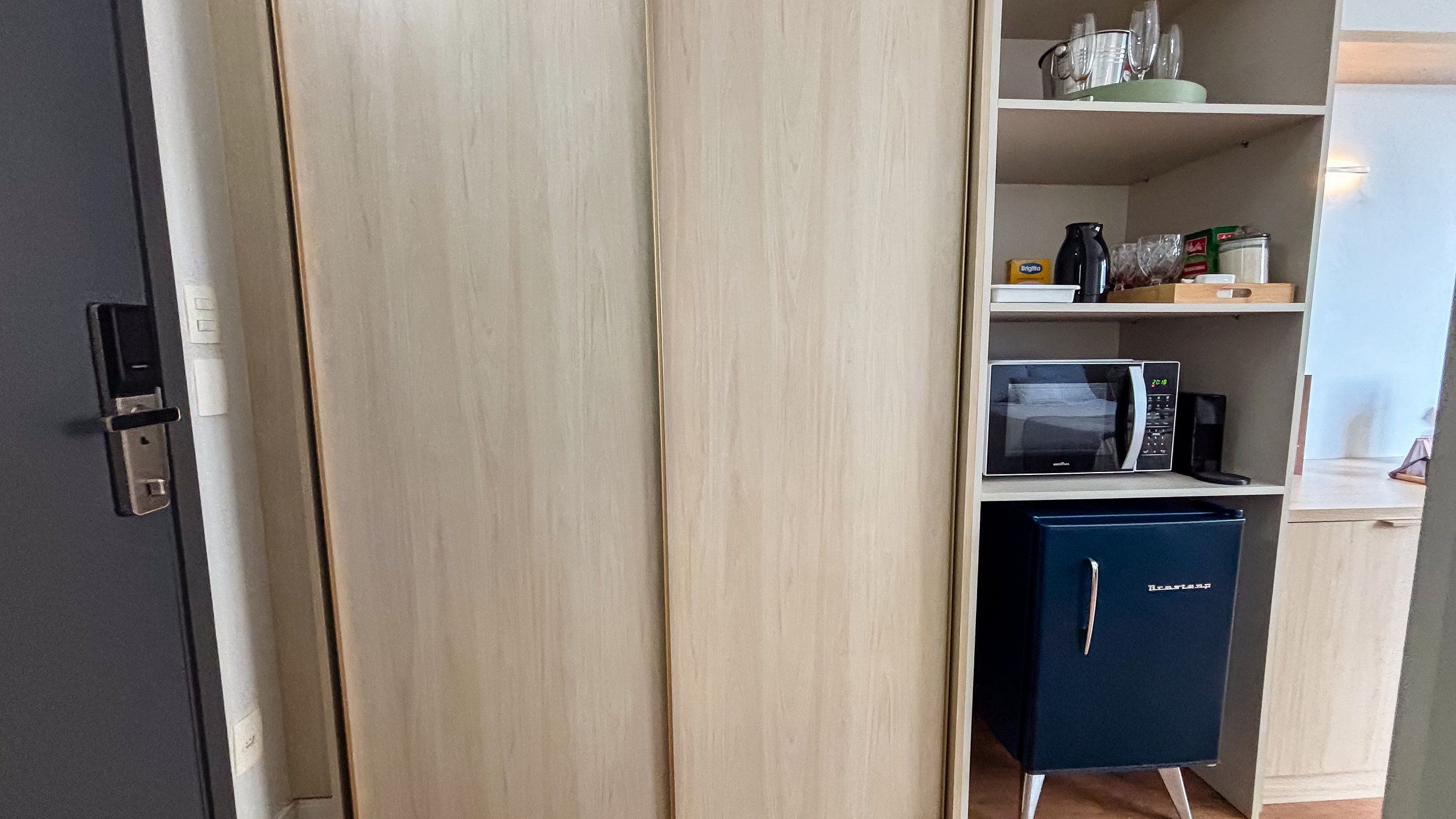 Una cocina con microondas, un refrigerador pequeño y una repisa con diversos artículos.