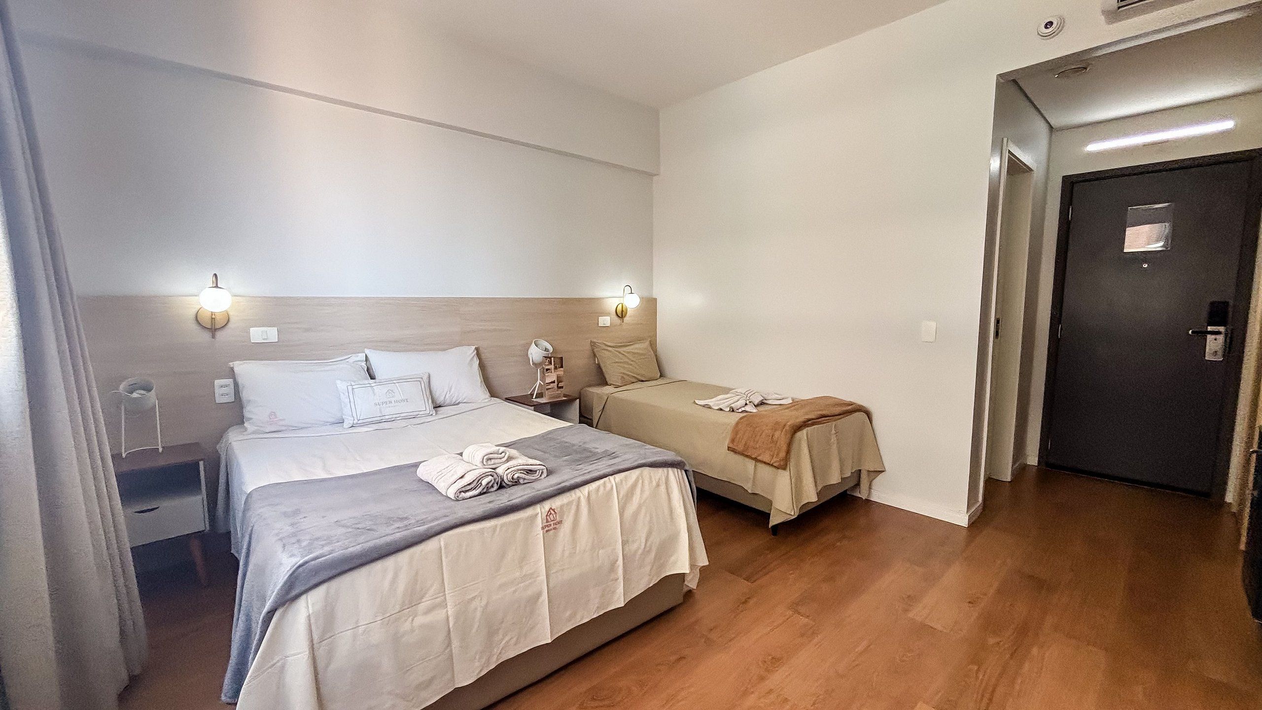 A hotel room with two beds, a bedside table with a lamp, and a door.
