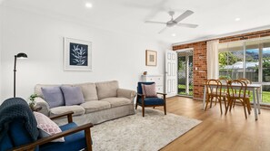 A living room with a sofa, armchairs, a dining table with chairs, a ceiling fan, and artwork on the walls. - Shoal Villa in Shoalhaven Heads (Shoalhaven Heads)