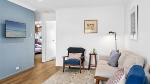 A living room with a sofa, a chair, a TV, and a painting on the wall. - Shoal Villa in Shoalhaven Heads (Shoalhaven Heads)