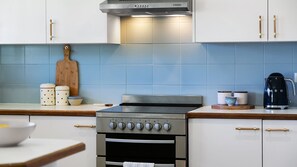 A kitchen with a stainless steel stove, wooden handles, and a blue tiled backsplash. - Shoal Villa in Shoalhaven Heads (Shoalhaven Heads)