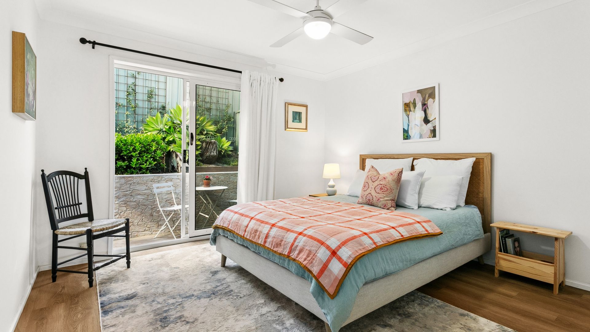 A bedroom with a bed, a chair, a nightstand, a lamp, and a view of the outdoors.