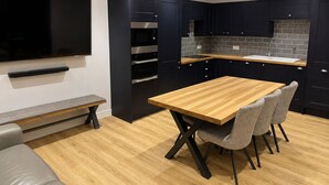A modern kitchen with dark cabinetry, a wooden dining table, and a bench. - Stylish 1 Bedroom Town Centre Flat in Saltash 5 Mins from Train Station (Saltash)