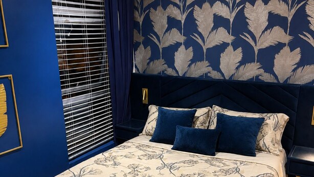 A bedroom with a bed, a nightstand, a window with blinds, and a wall with a leaf pattern. - Stylish 1 Bedroom Town Centre Flat in Saltash 5 Mins from Train Station (Saltash)