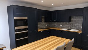 A modern kitchen with dark cabinetry, a wooden countertop, and a built-in oven. - Stylish 1 Bedroom Town Centre Flat in Saltash 5 Mins from Train Station (Saltash)