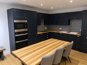 A modern kitchen with dark cabinetry, a wooden countertop, and a built-in oven. - Stylish 1 Bedroom Town Centre Flat in Saltash 5 Mins from Train Station (Saltash)