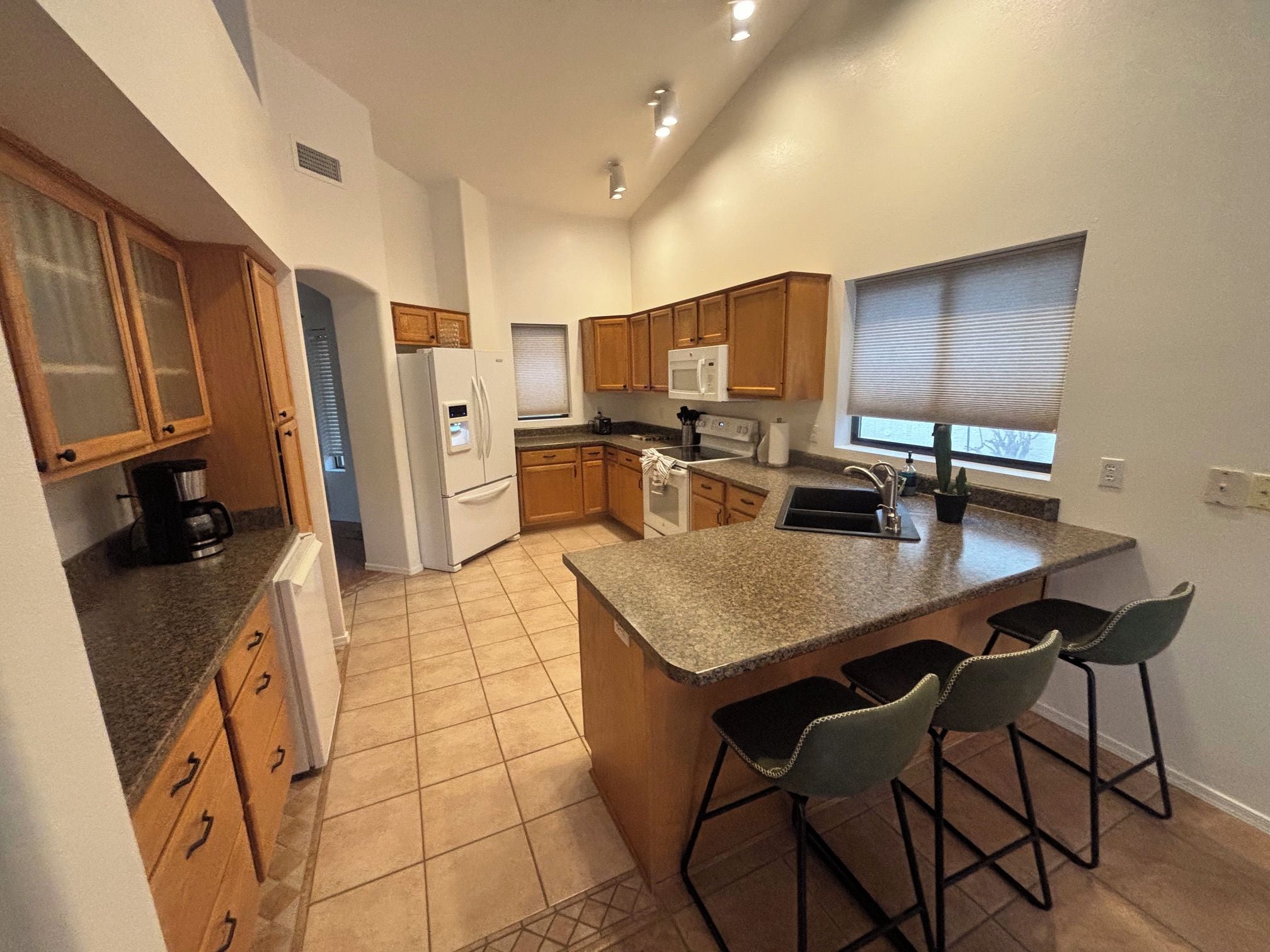 A modern kitchen with a central island, bar stools, wooden cabinets, and a built-in microwave.