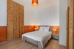 Une chambre avec une armoire en bois, un lit avec une literie blanche, deux lampes de chevet et un plancher en bois.