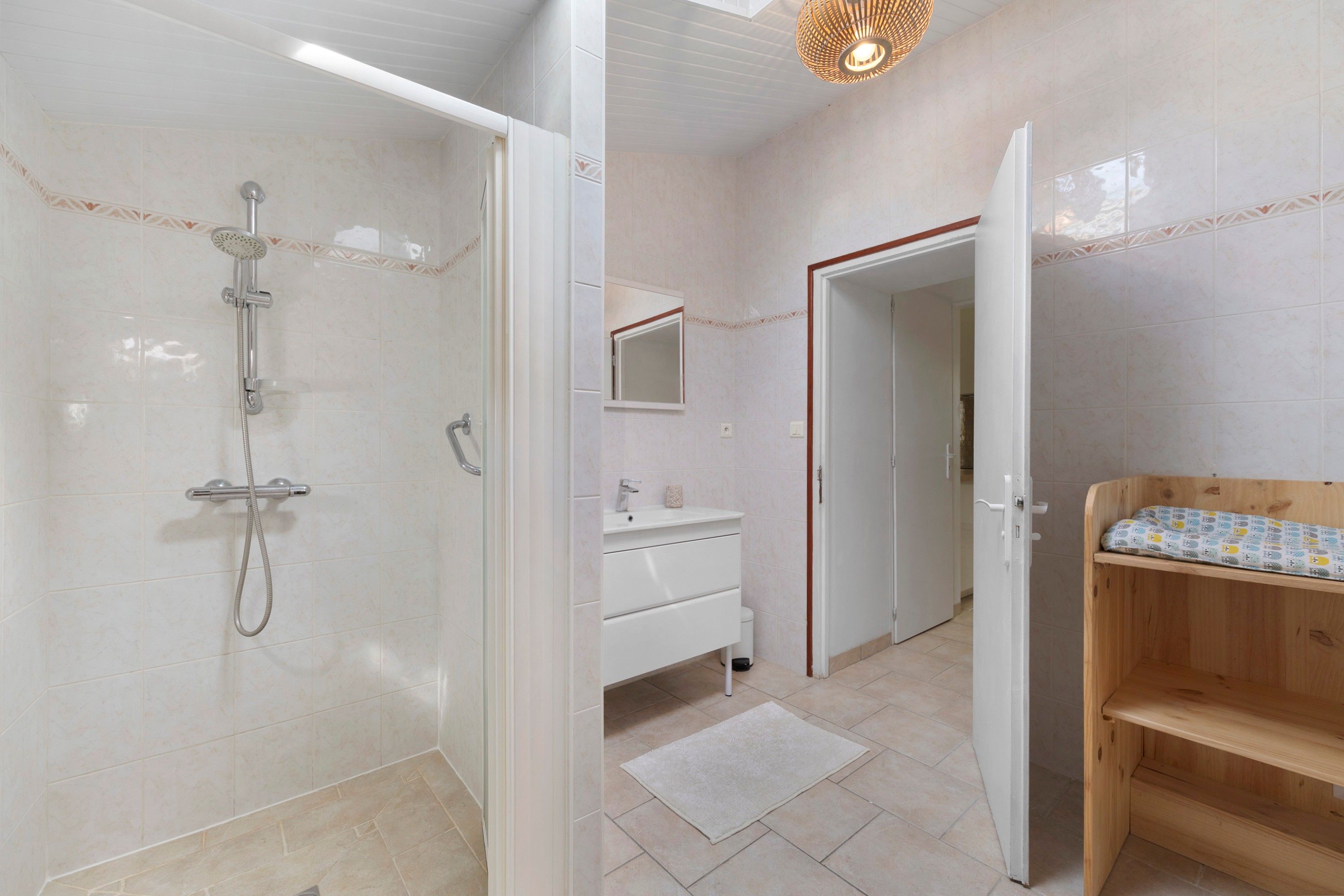 Een moderne badkamer met een douche, een wastafel en een houten bankje.