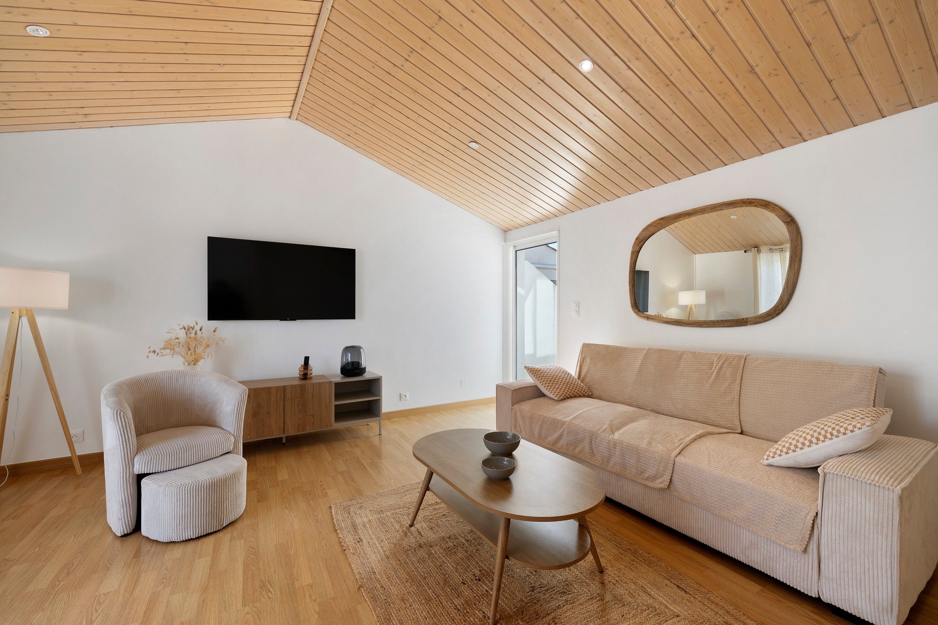 A modern living room with a wooden ceiling, a flat-screen TV, a sofa, a coffee table, and a side table.