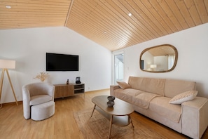 Un salon moderne avec un plafond en bois, un téléviseur à écran plat, un canapé, une table basse et une table d’appoint.