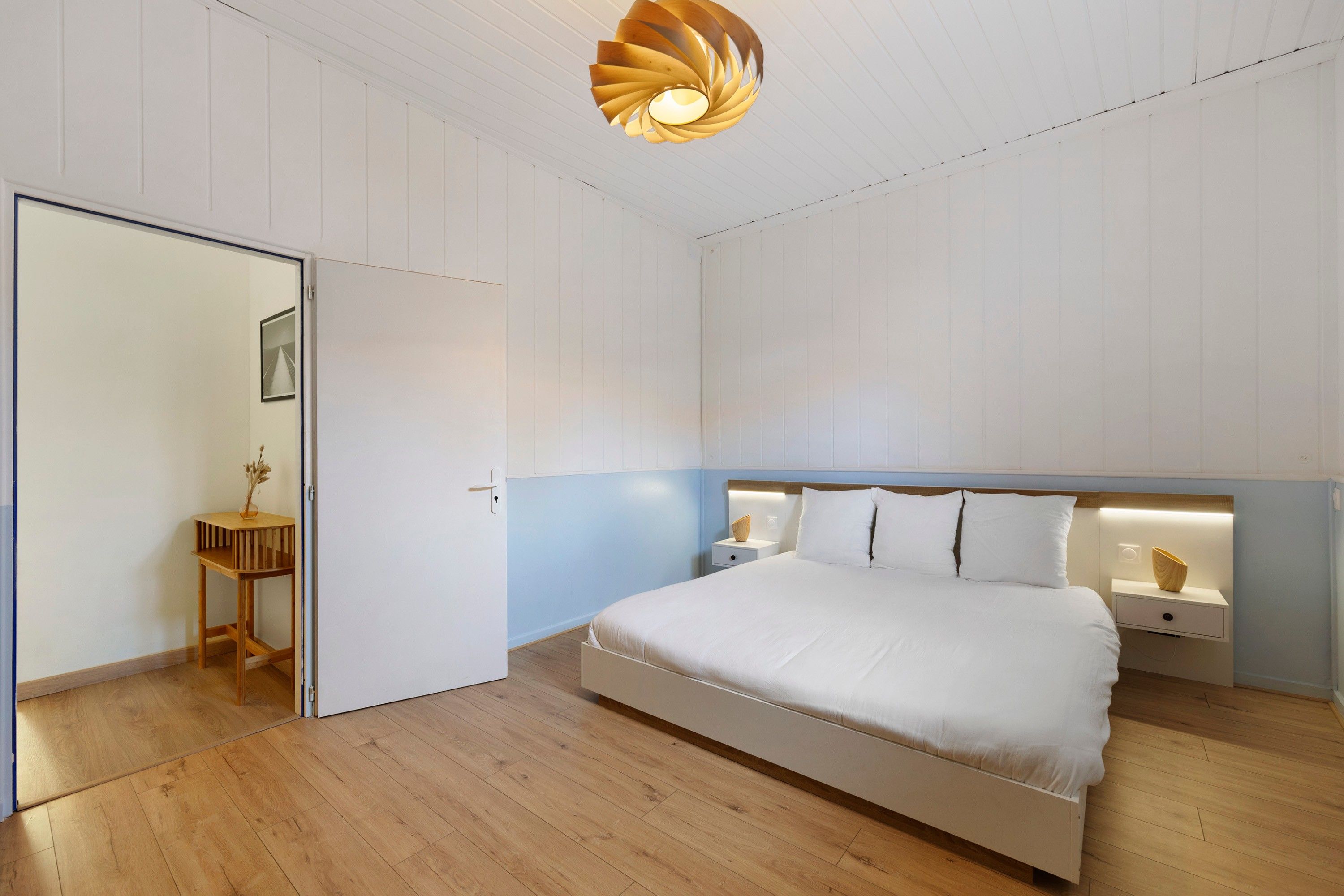 Una camera da letto con un letto, comodini, pavimento in legno e un originale lampadario.