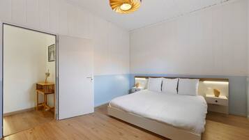 A bedroom with a bed, bedside tables, a wooden floor, and a unique ceiling light fixture.