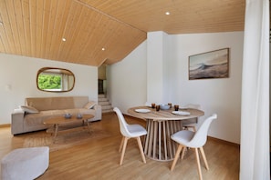 Un intérieur moderne avec un plafond en bois, une table à manger ronde entourée de chaises, un canapé et un tableau accroché au mur.