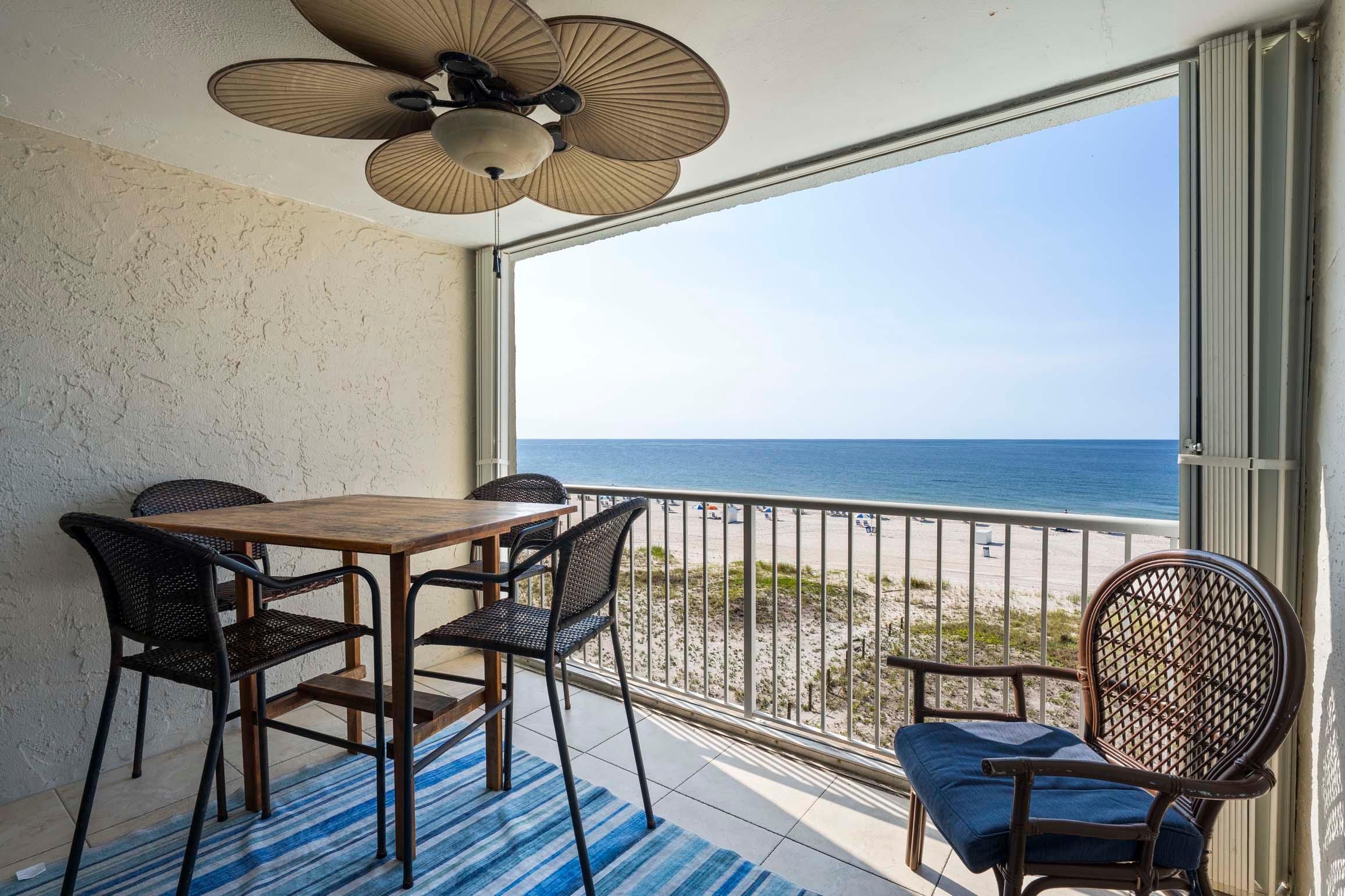 A balcony with a table and chairs, a view of the ocean, and a ceiling fan.