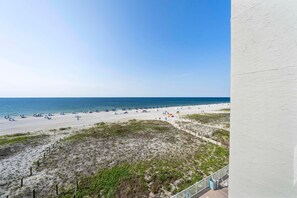 A beach with umbrellas and a flag, a clear sky, and a view of the ocean. - Castaways 4A (Gulf Shores)