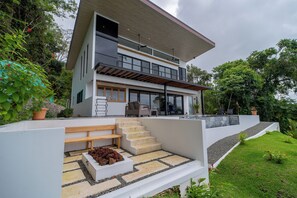 Una casa moderna de dos pisos con techo plano, ventanas amplias y un balcón.