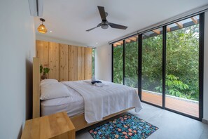A modern bedroom with a large bed, wooden headboard, and a view of lush greenery through floor-to-ceiling windows. - Modern family friendly, ocean view house near Dominical - Wi-Fi, inifinity pool (Dominical)
