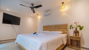 A hotel room with a bed, a ceiling fan, a flat-screen TV, and a bedside table with a plant. - Modern family friendly, ocean view house near Dominical - Wi-Fi, inifinity pool (Dominical)