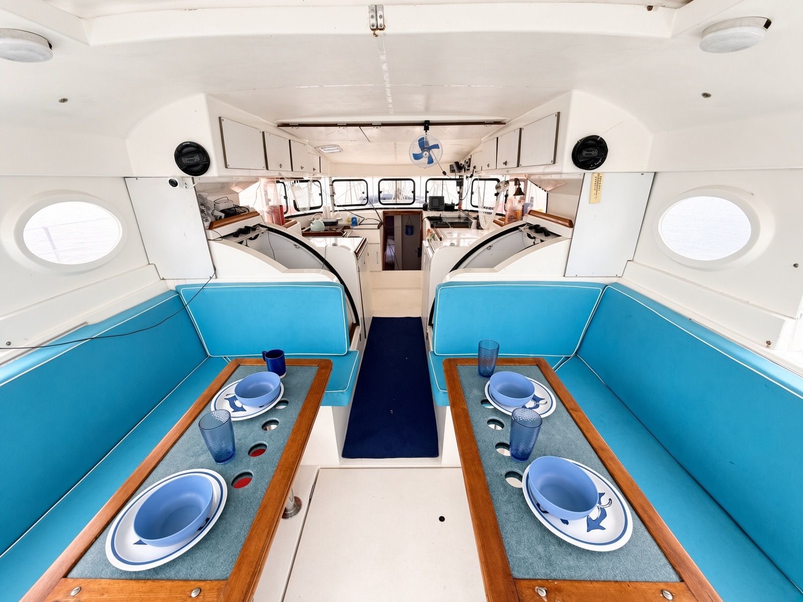 Interior de un barco con dos zonas de comedor, cada una con una mesa, sillas y un pasillo central.