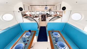 Interior de un barco con dos zonas de comedor, cada una con una mesa, sillas y un pasillo central.