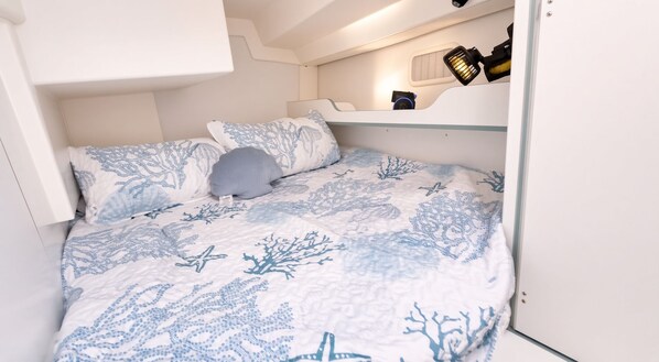 A compact bedroom with a bed, pillows, and a small shelf with a lamp.