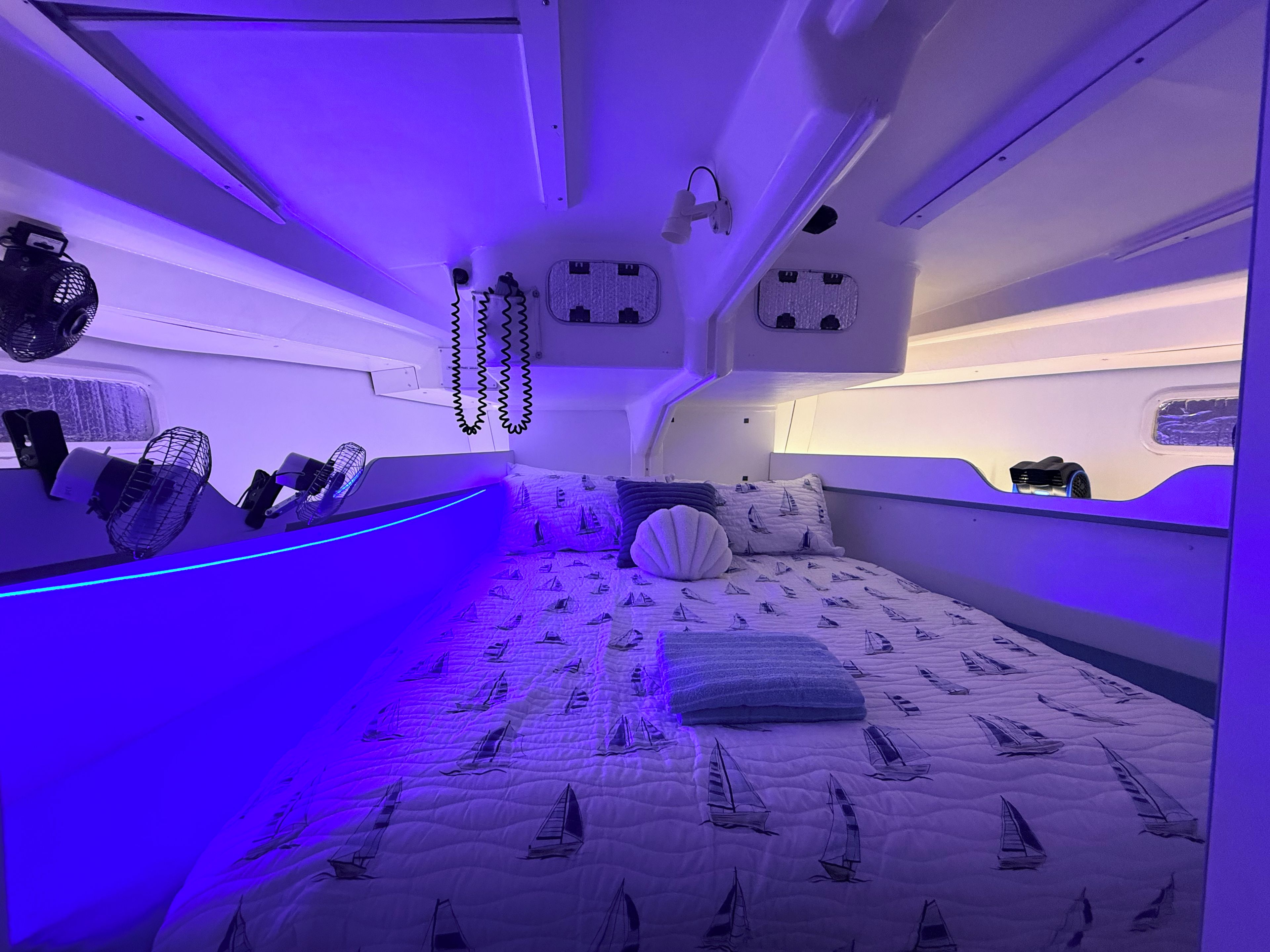 Quarto com cama estampada com tema náutico, mesa de cabeceira com abajur e ventilador fixado na parede.
