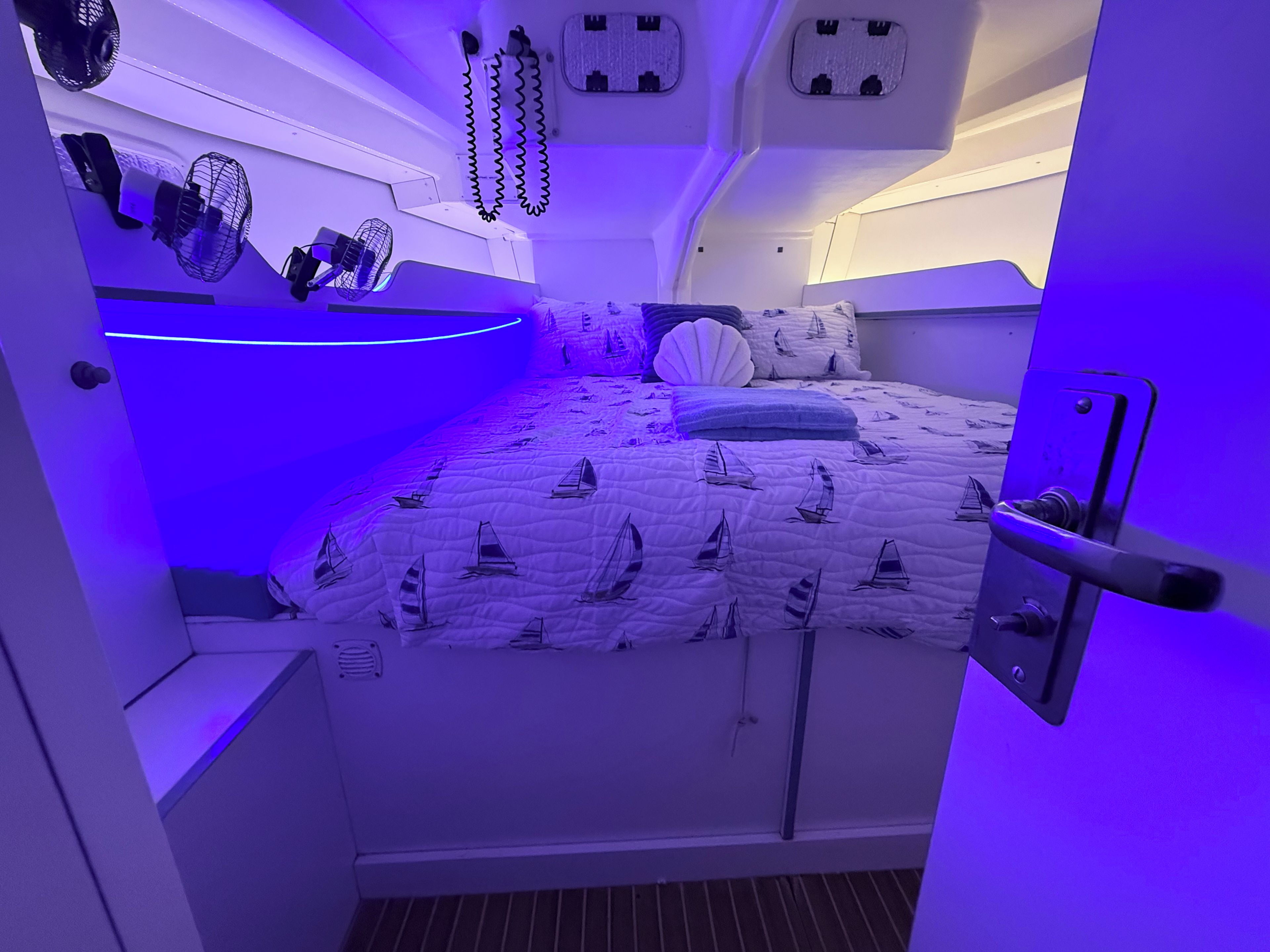 Una camera compatta con un letto a disegno con barca a vela, una piccola scrivania e una ventola a parete.