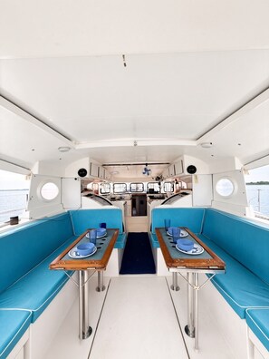 Interior de un barco con dos mesas y asientos acolchados azules.