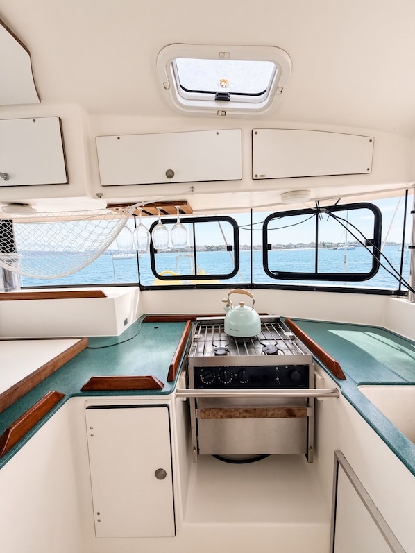 A boat's interior with a galley area, a small window with a view of the water, and a hammock.