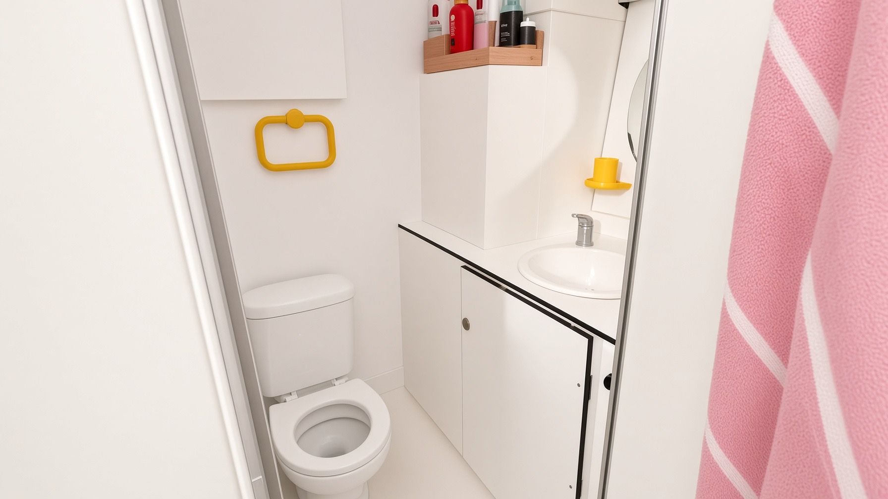 Une petite salle de bain moderne, équipée de toilettes, d’un lavabo et d’étagères de rangement.
