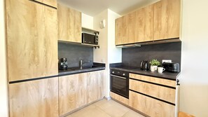 Eine moderne Küche mit Holzschränken, einer schwarzen Arbeitsplatte, einer Kaffeemaschine, einem Wasserkocher und einem Toaster.