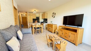 Ein modernes Wohnzimmer mit Sofa, Fernseher, Esstisch aus Holz und einer Küche im Hintergrund.