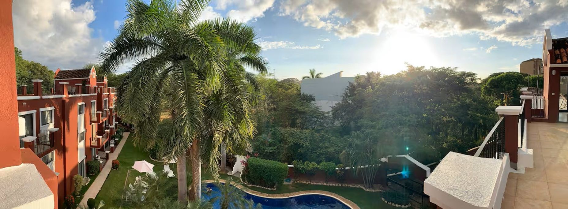 A residential area with a swimming pool surrounded by lush greenery and palm trees.